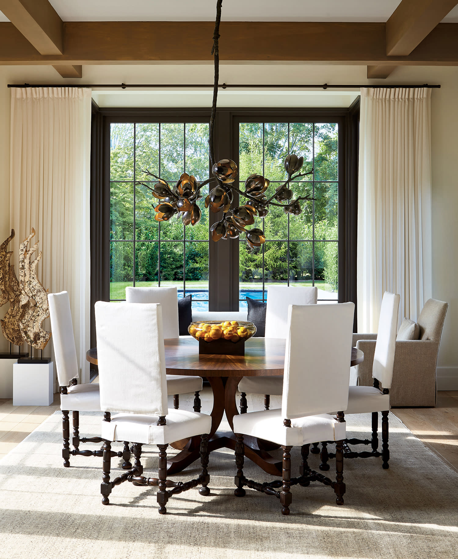 a bronze floral chandelier hangs above a dining table surrounded with vintage Italian chairs