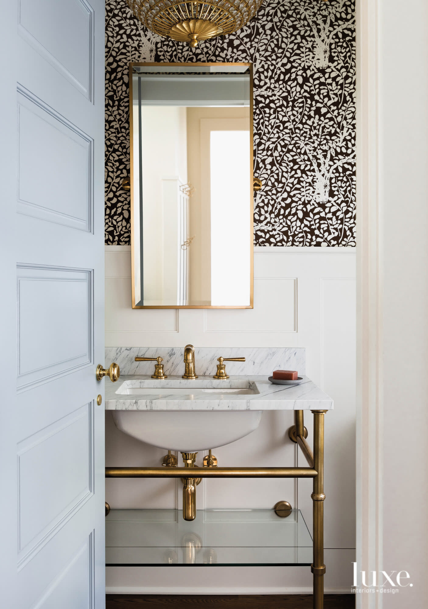 Powder room with a black and white patterned wallpaper, wainscot and brass finishes.
