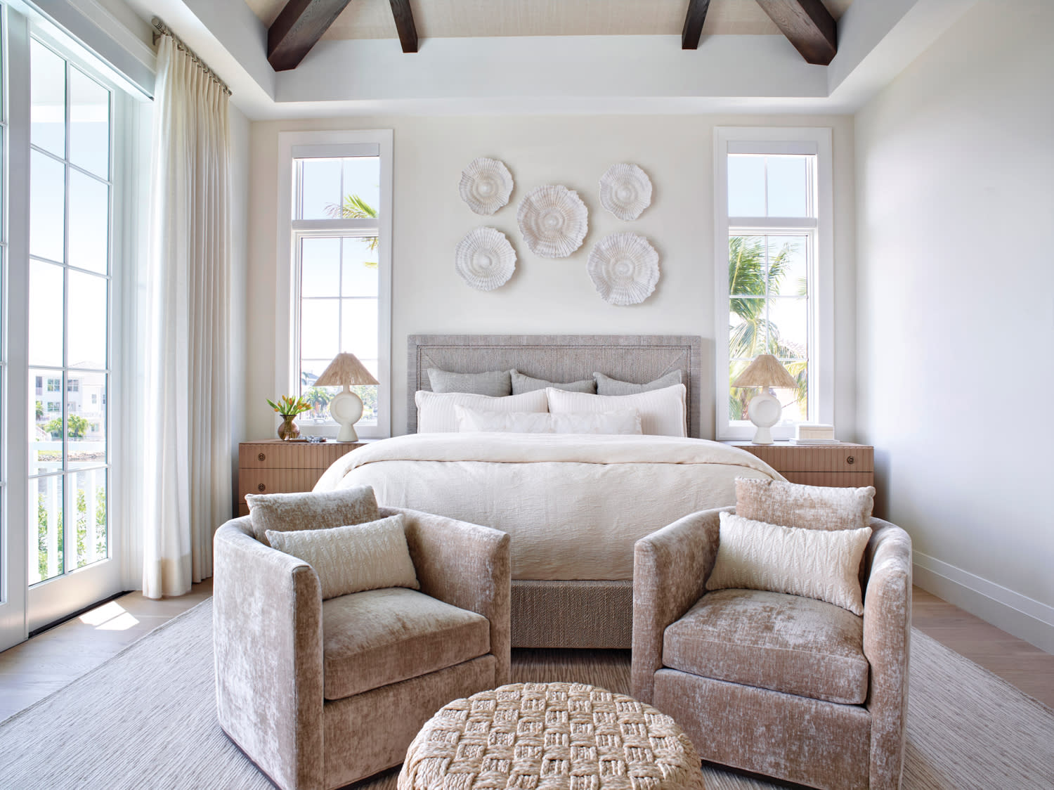 white, airy bedroom with a pair of pale pink armchairs in front of a Palacek bed