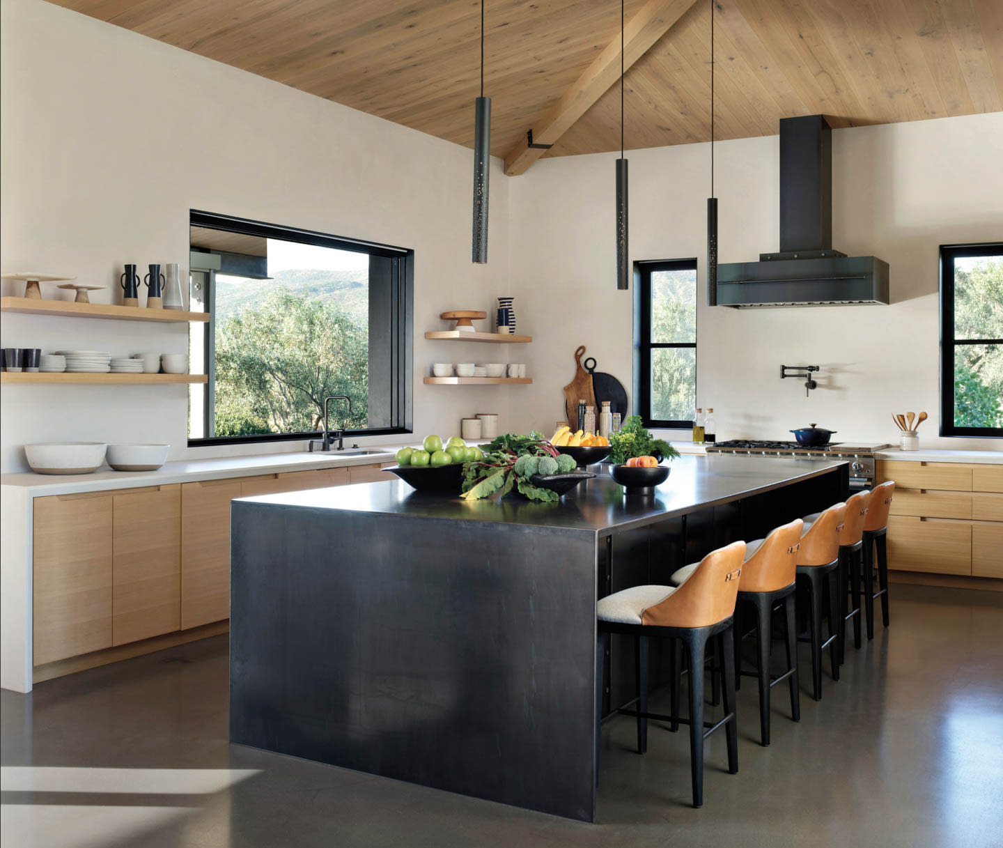 Modern kitchen with a sleek black island, wooden bar stools, and open shelving. Natural light pours in through large windows, creating a warm, inviting atmosphere.