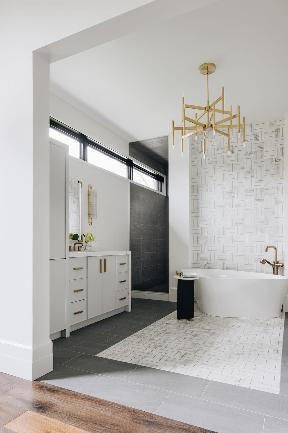 This black and white primary bathroom with white soaker tub, decorative white tile inlay that runs along the center of floor and up the wall behind tub.