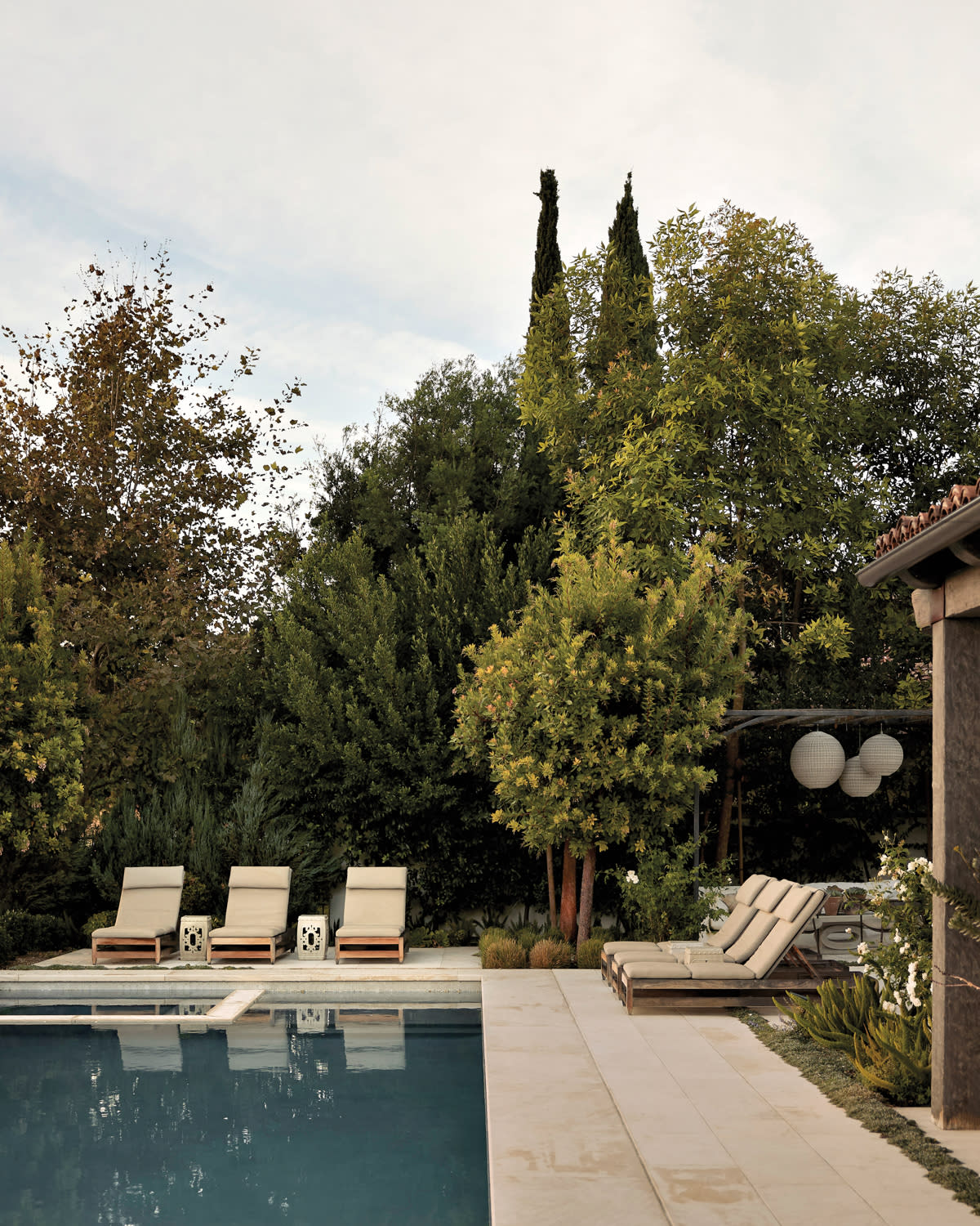 pool in tree-filled backyard surrounded by lounge chairs with vintage Chinese garden stools between each chair by Nicole Green