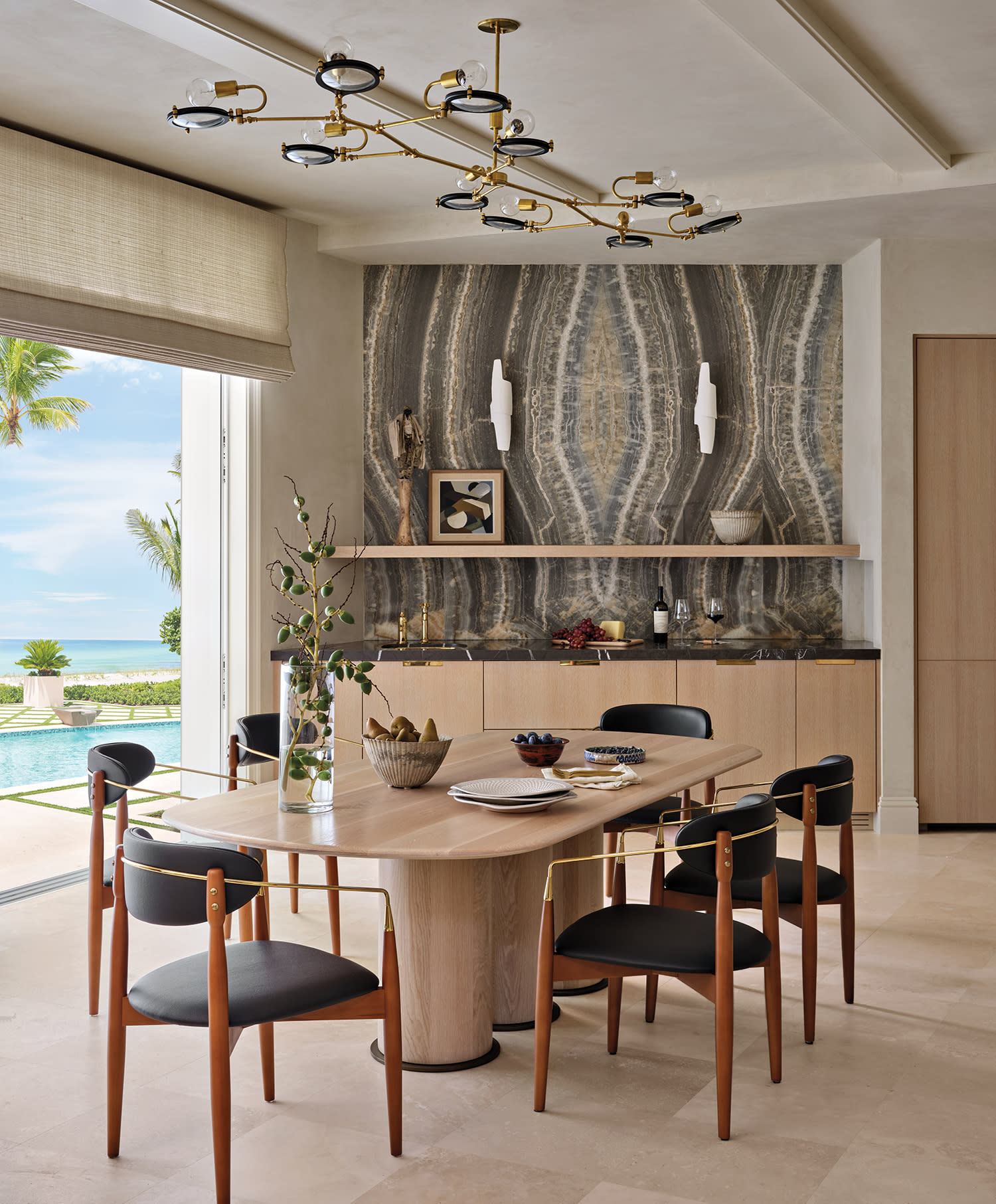 Sophisticated dining room with a wooden table, chairs, modern chandelier, and large stone accent wall.