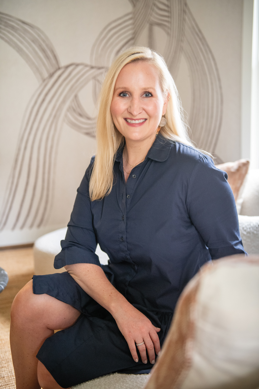 Alexis Pearl in a navy-blue button-down dress sitting on a couch