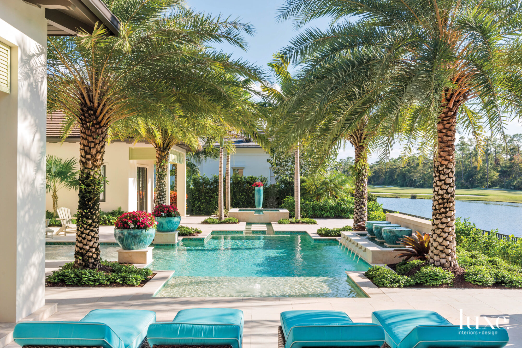 Turquoise chaises overlooking a pool surrounded by palm trees.