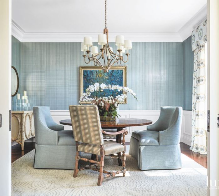 The formal dining room includes a Bausman & Company table, a Niermann Weeks chandelier, and chairs wearing Kravet Couture fabric. Phillip Jeffries’ wallcovering from Holly Hunt backs a painting by Bruno Zupan. Draperies are by leejofa.com, the rug is from J. Namnoun Oriental Rug Gallery in Connecticut, and the cabinet is by Michael Taylor Designs. An orchid from Floral Emporium brings the outside in.