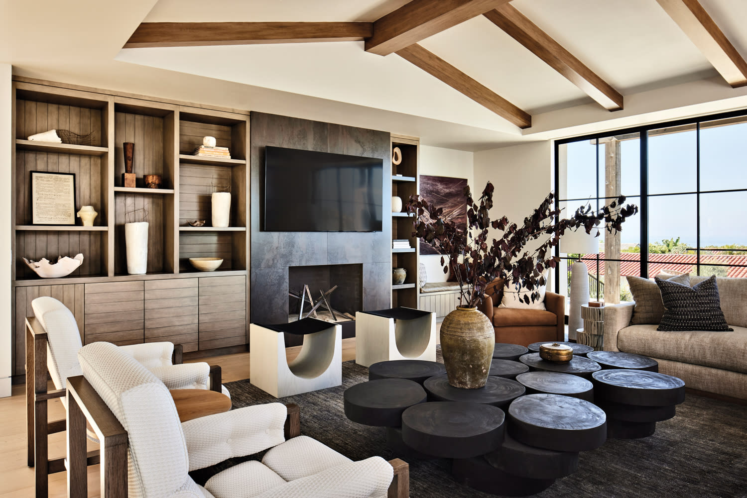 living room with coffee table made from varied round wooden pieces, flanked by two chairs, two paddle stools and a sofa, with a fireplace and built in shelving in the background