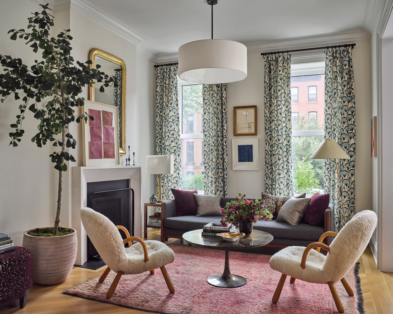 Cozy living room with a gray sofa, patterned curtains, and two plush chairs around a round coffee table. Soft lighting and art create a welcoming ambiance.