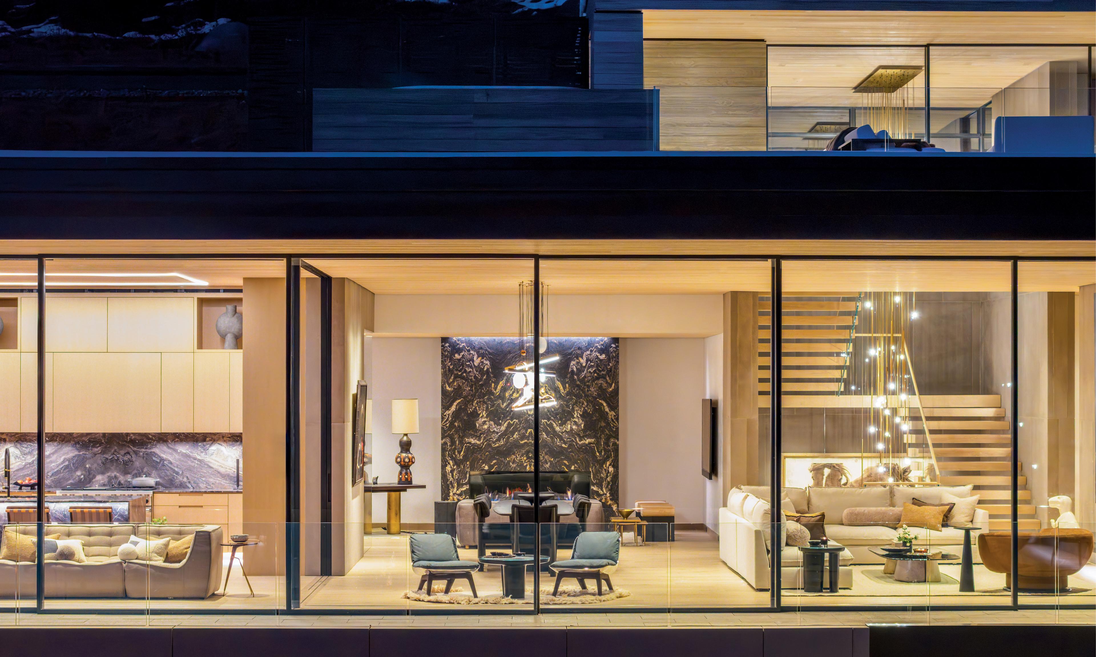 Modern home interior with large glass windows, showcasing a living area, dining space, and kitchen. Warm lighting creates an inviting, luxurious atmosphere.