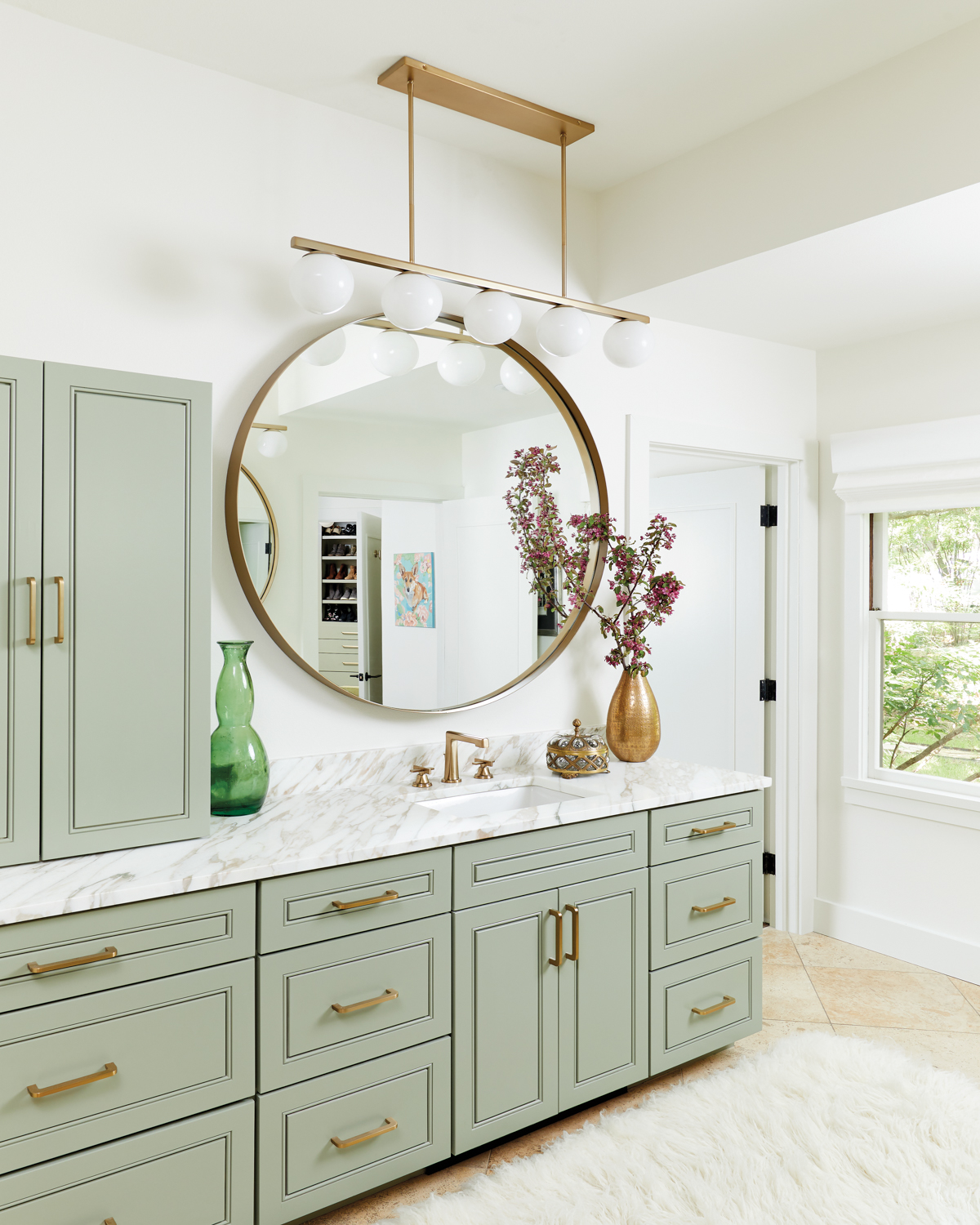 sage green bathroom cabinetry topped with marble counters and brass accents