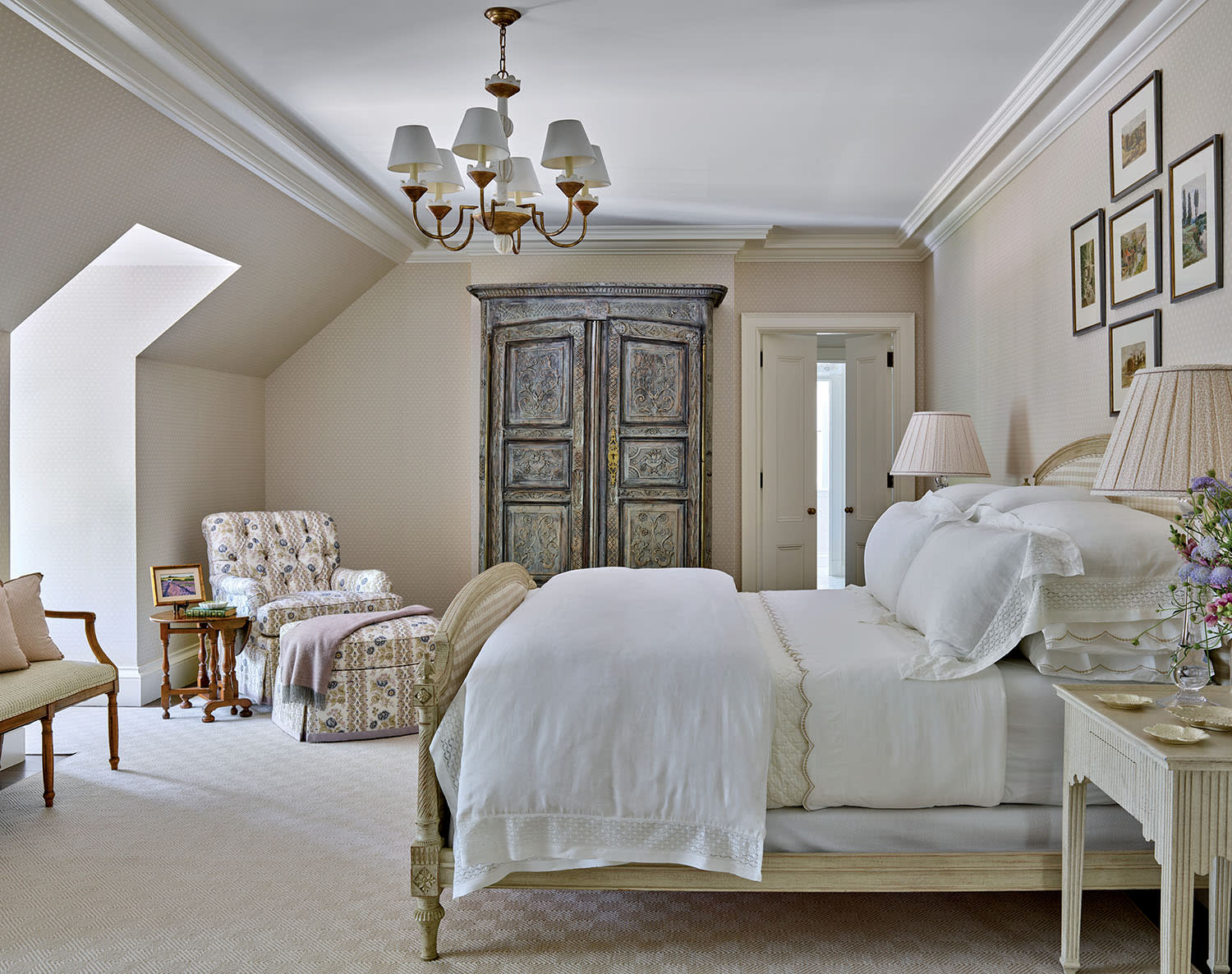 Elegant bedroom with a vintage vibe, featuring a wooden bed with white bedding, an ornate wardrobe, floral armchair, and pastel decor. Tone is serene and cozy.
