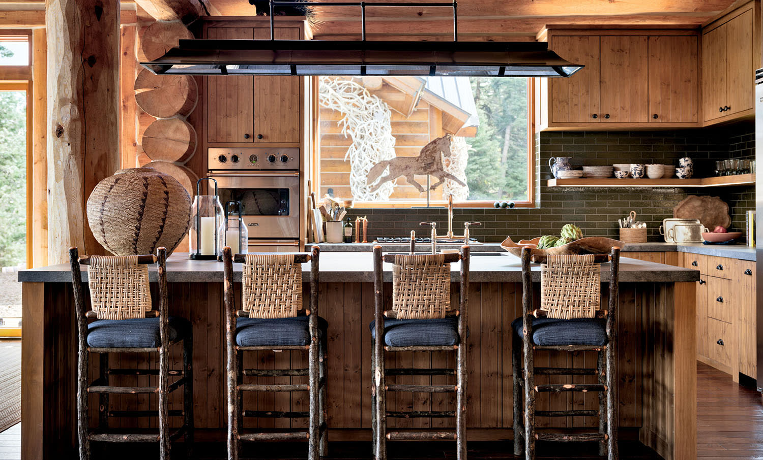 Four high-top chairs with woven backs and navy cushions sit at the island in a kitchen with wood cabinetry.