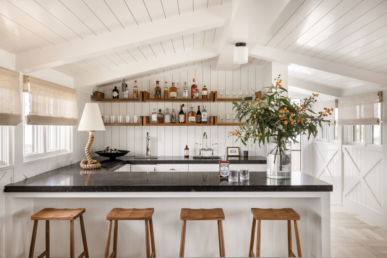 home bar with open shelving, black granite countertops, backless counter stools and table lamp with a nautical-style rope base