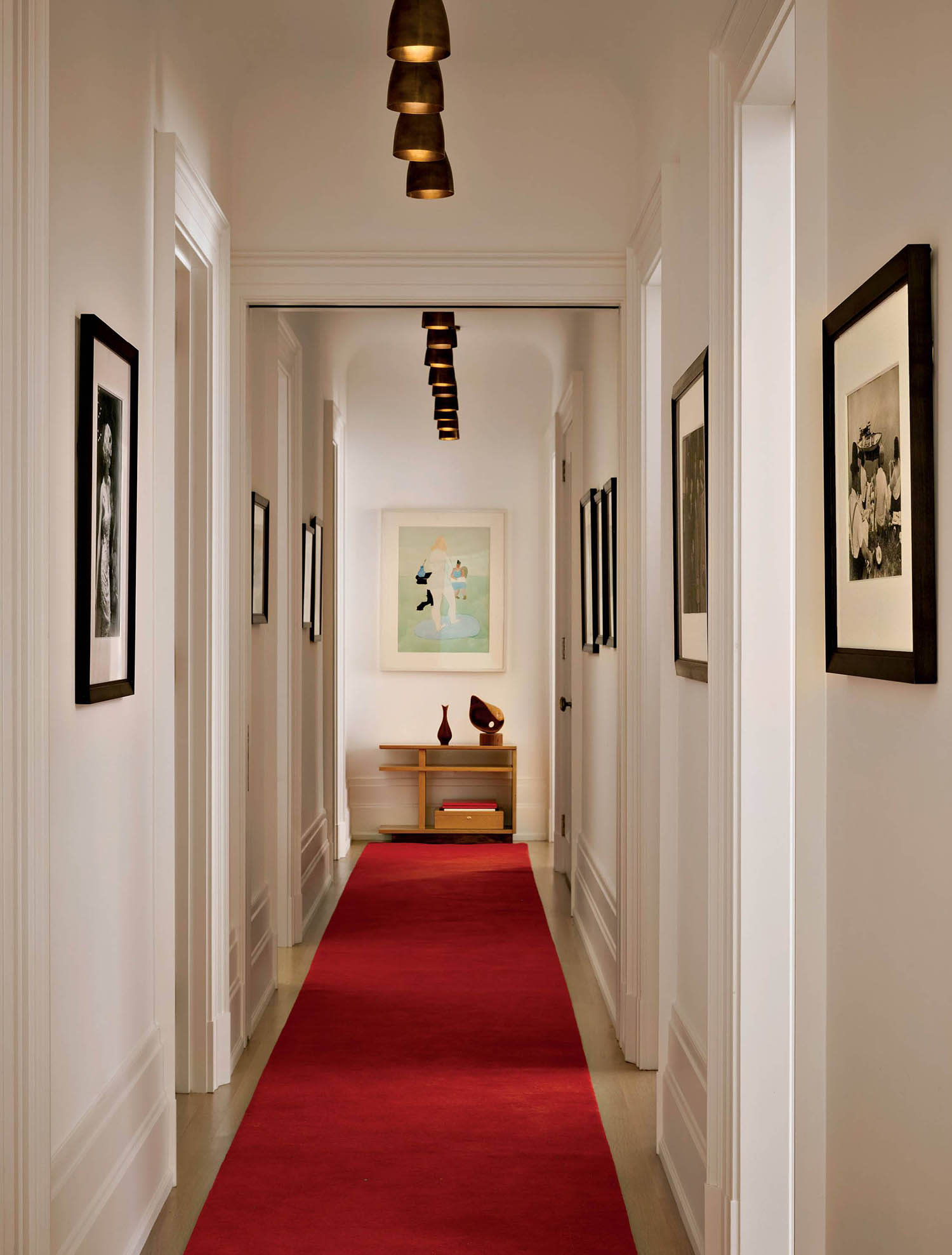 A red rug runs down a long hallway with framed photography hanging on white walls.