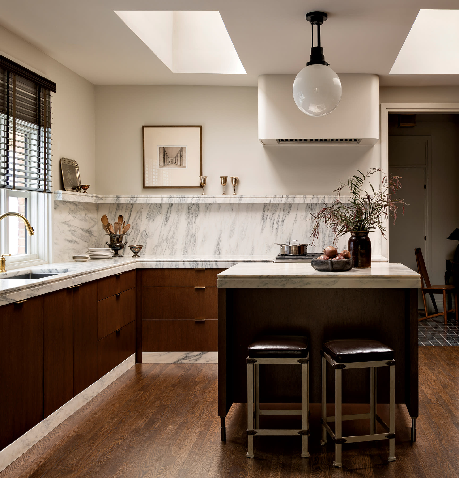 warm wood cabinetry lines the kitchen and its island under gray and white marble countertops