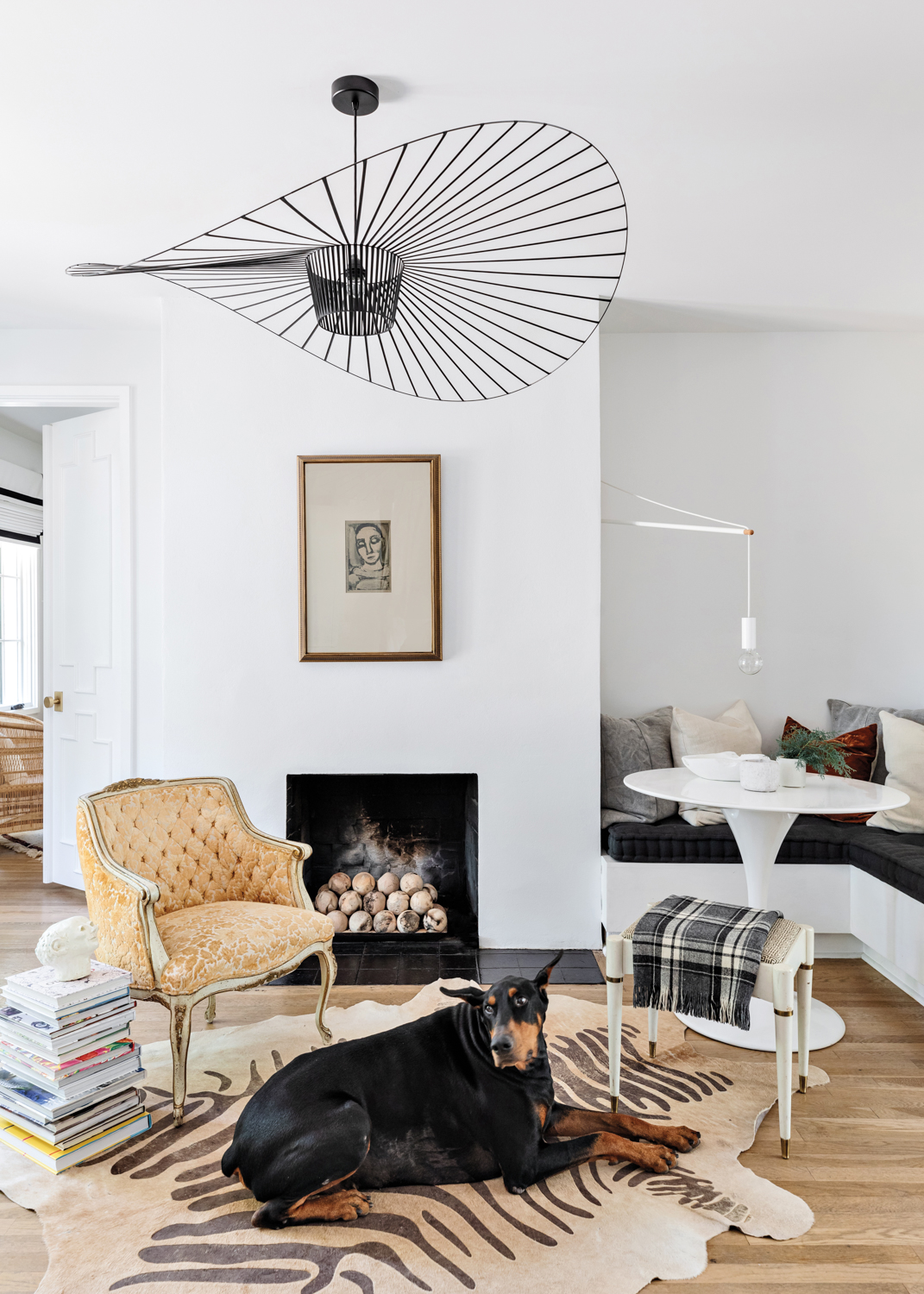 A dog lays on wood floors in living area with all-white ceiling next to dining nook with built-in banquette