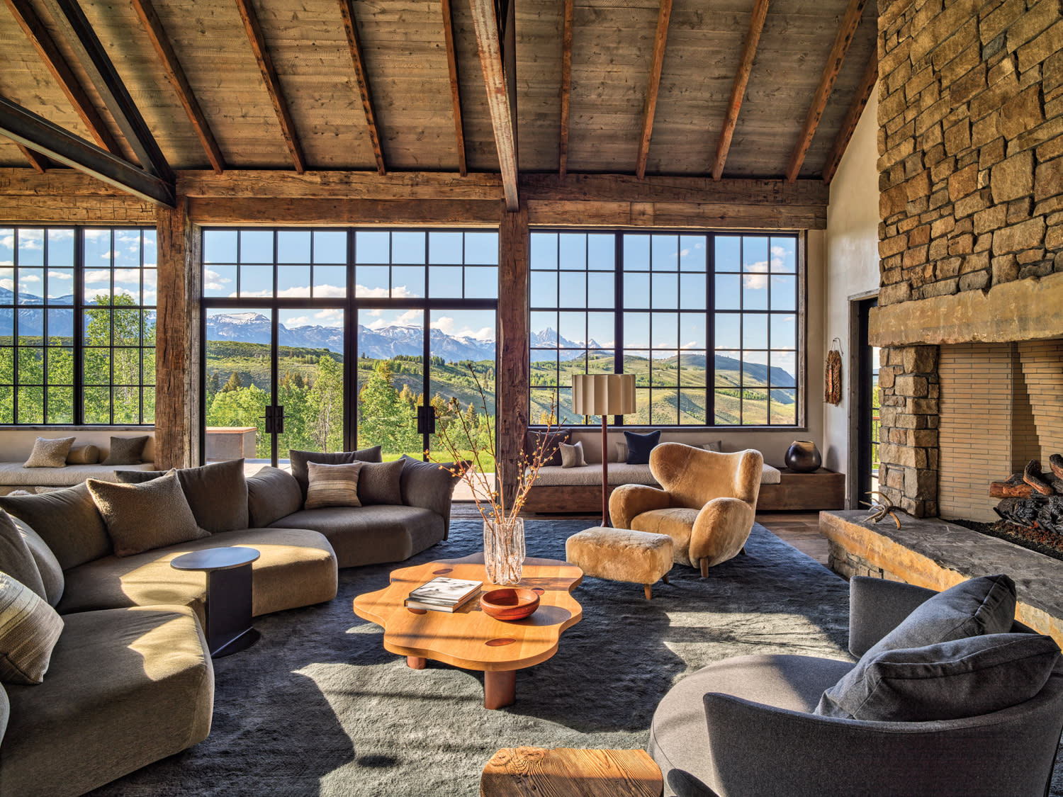 A cozy living room featuring a stone fireplace and large windows that allow natural light to fill the space.