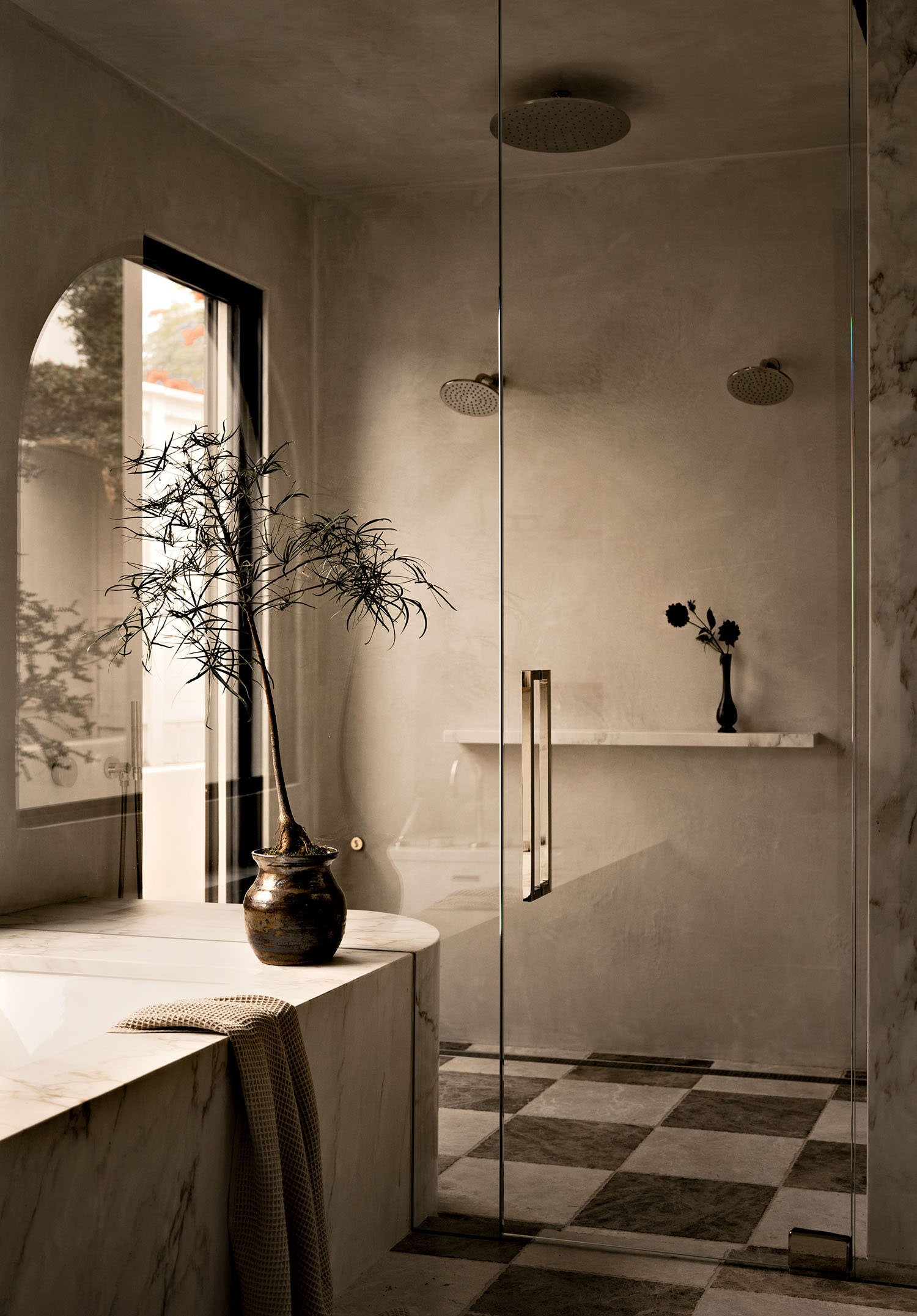 A marble bathtub sits next to a walk-in shower with built-in shelves and black-and-white floor tile.