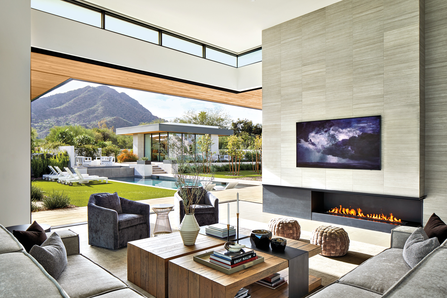 Living room with walls open to the backyard and views of a casita and mountains in home by Laura Kehoe