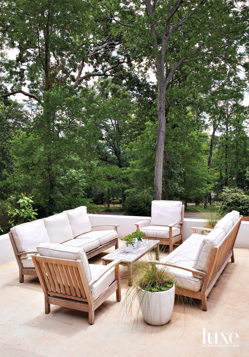 Outdoor seating group of teak furniture, tall stand of trees in the background