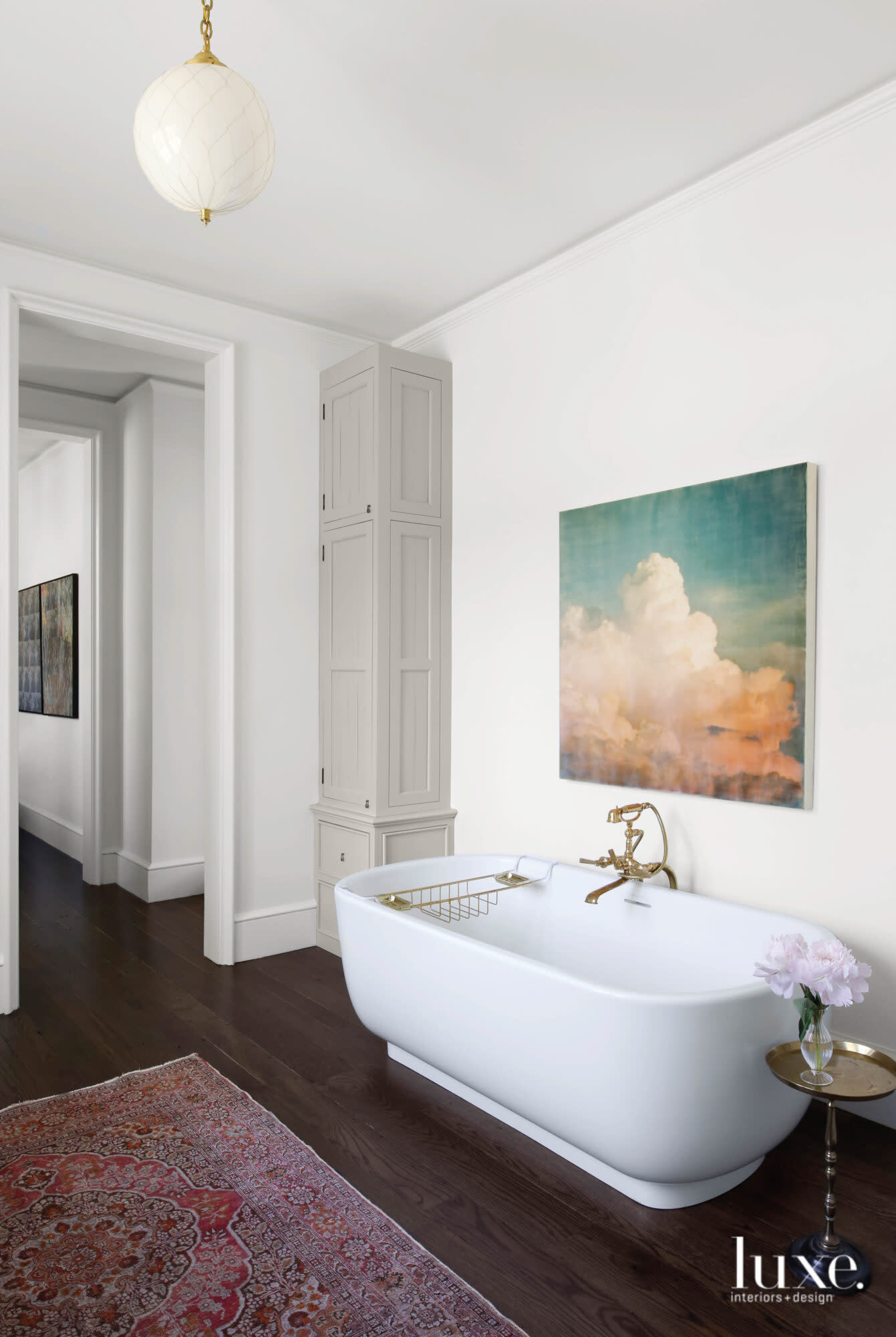 A bathtub, wood floors, pink rug and painting of clouds make up the master bathroom