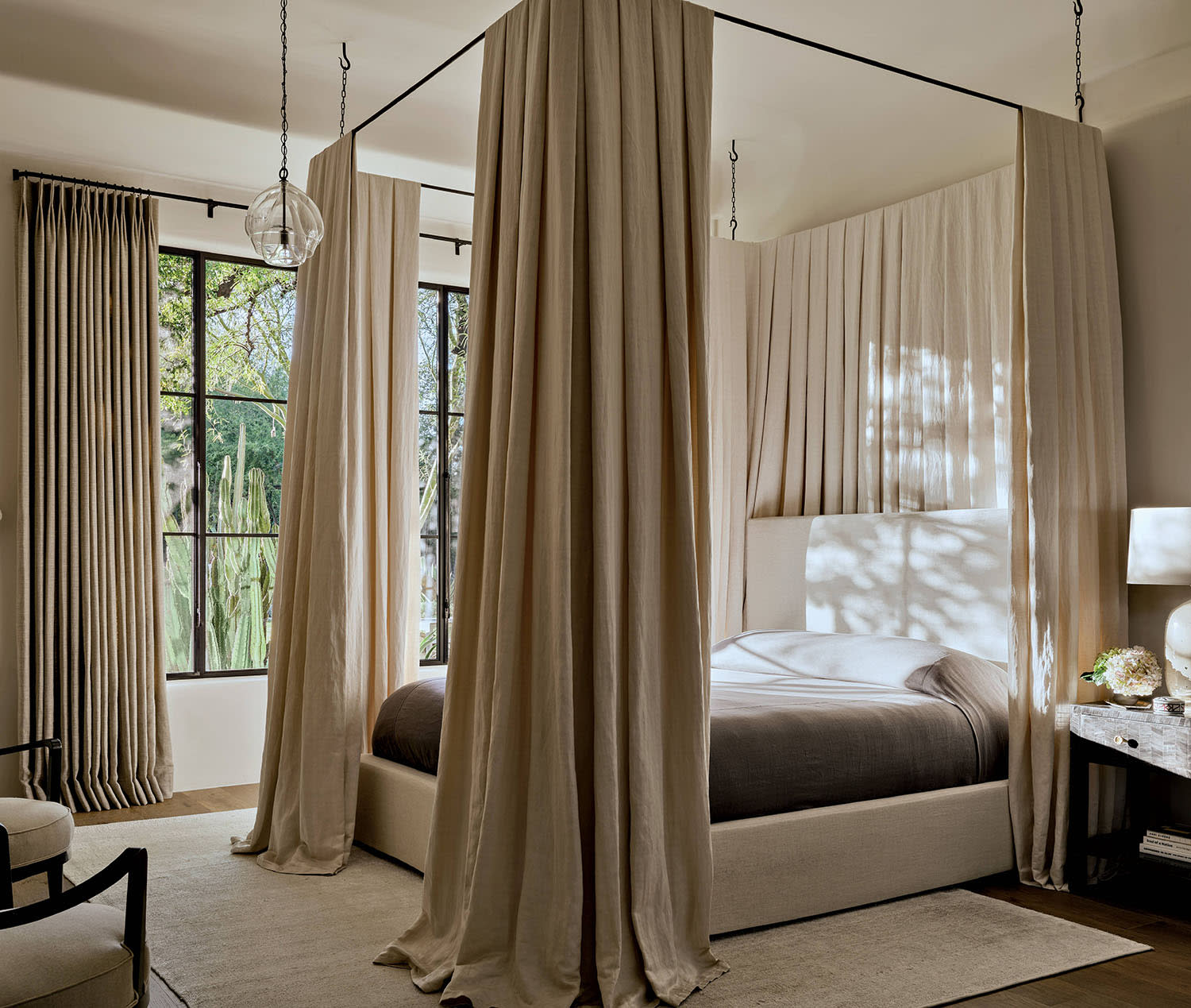 A canopy bed with curtains sits on a white rug with two chairs and a window looking outside.