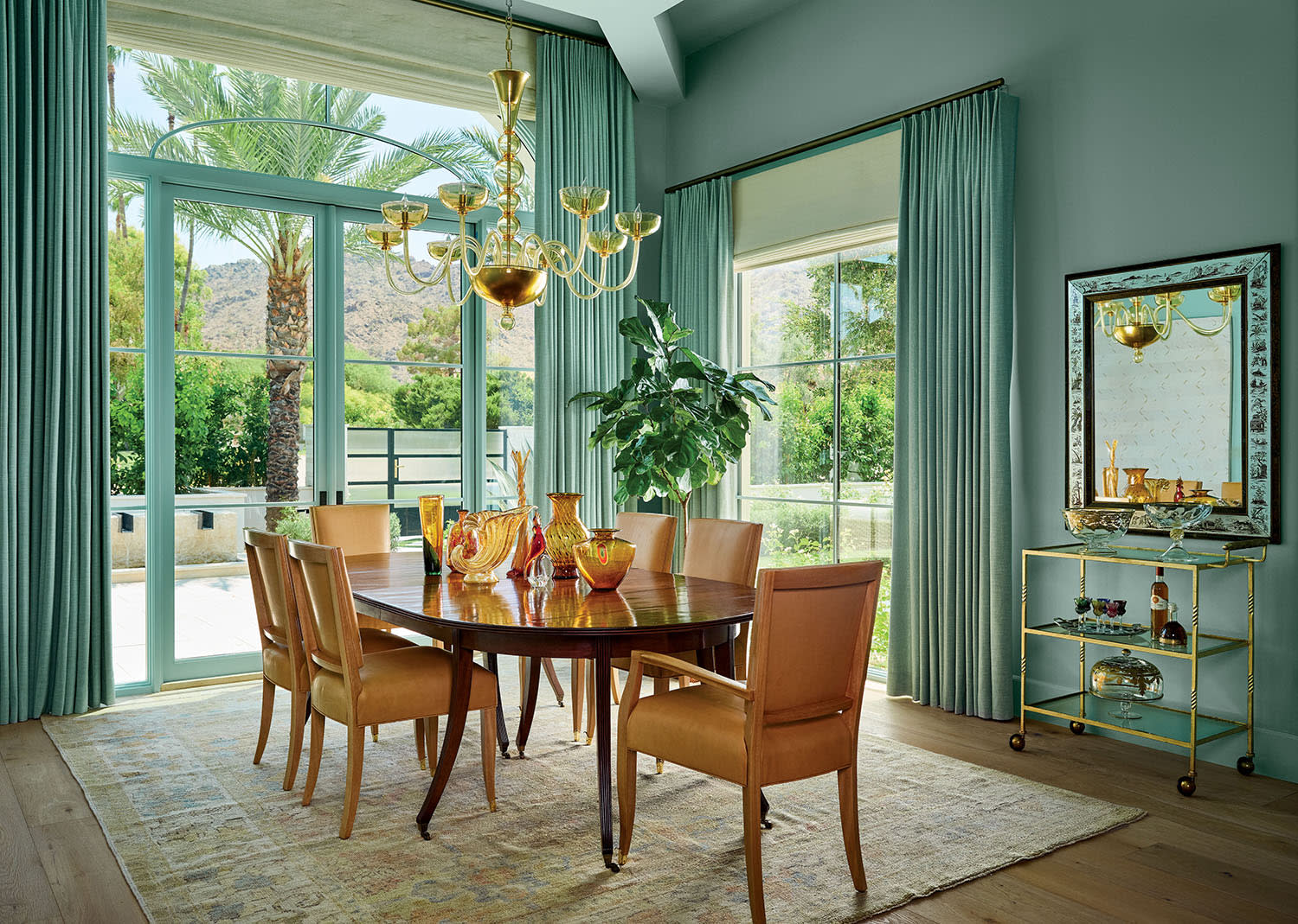 Elegant dining room with a large wooden table, surrounded by tan chairs with a gold chandelier above