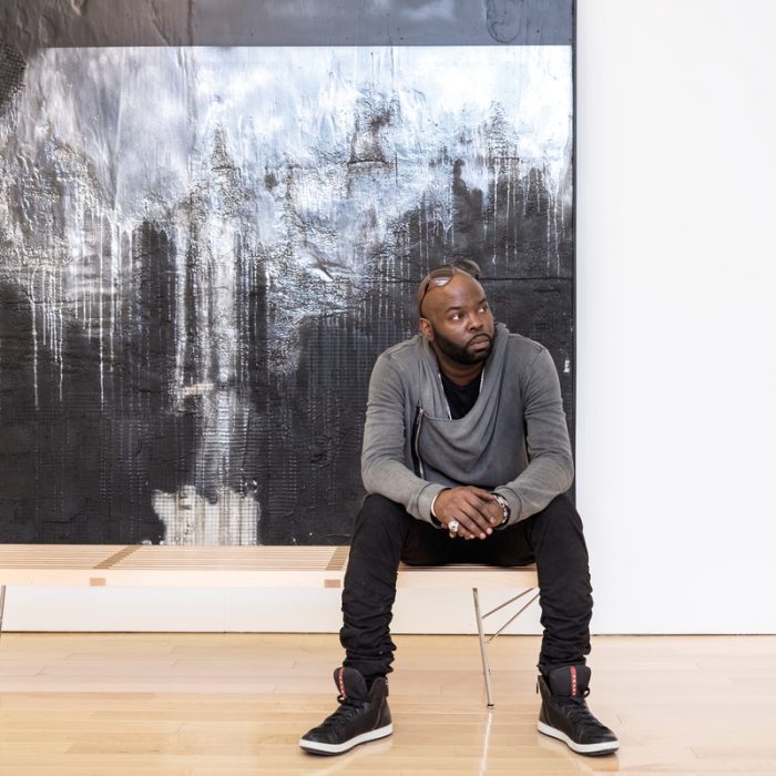 Dean sits in front of Number 74, a mixed-media piece on view in his exhibition "Recto/Verso: Duality of a Fragile Ego."