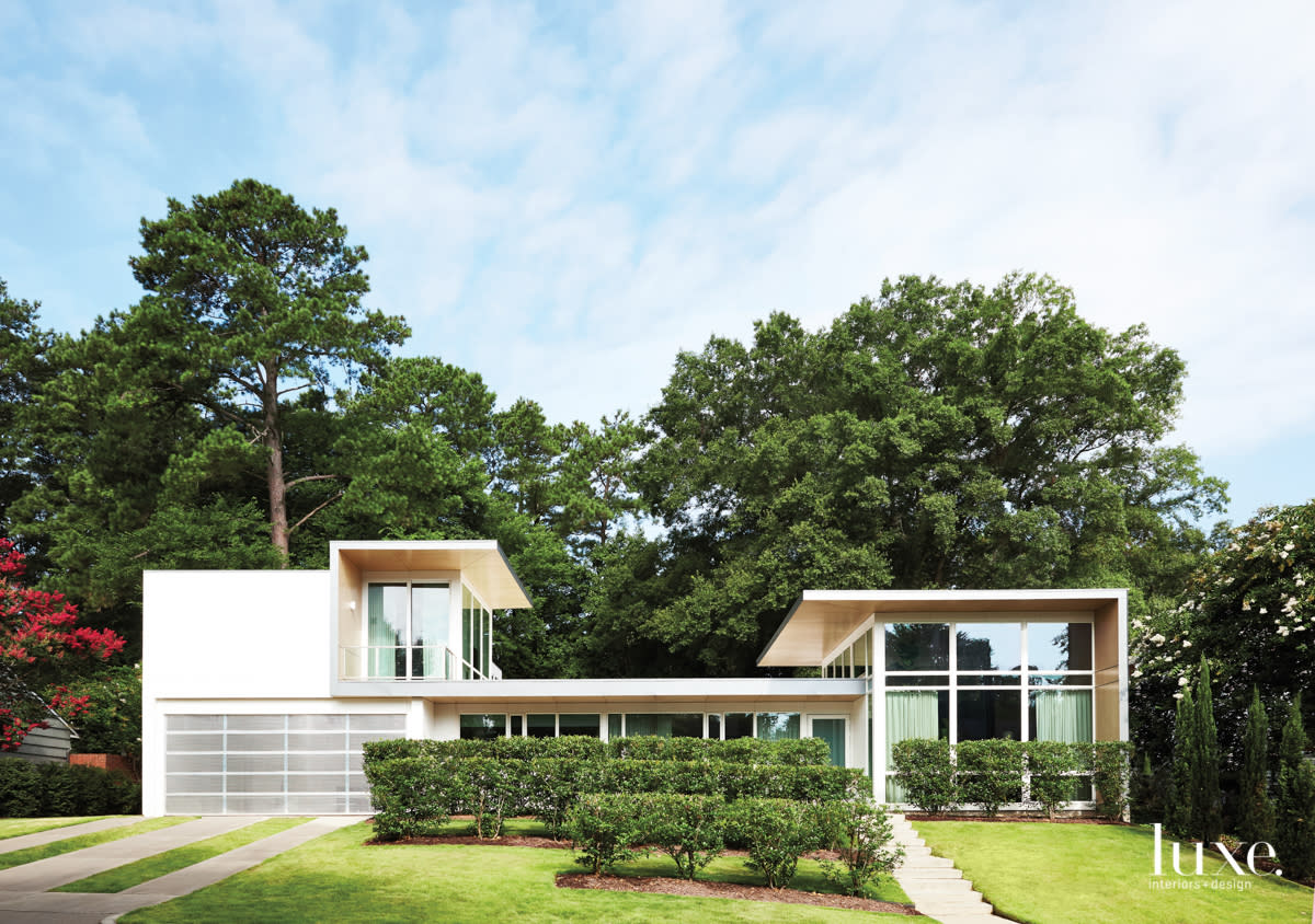 a white modern house framed by tall trees and a green lawn