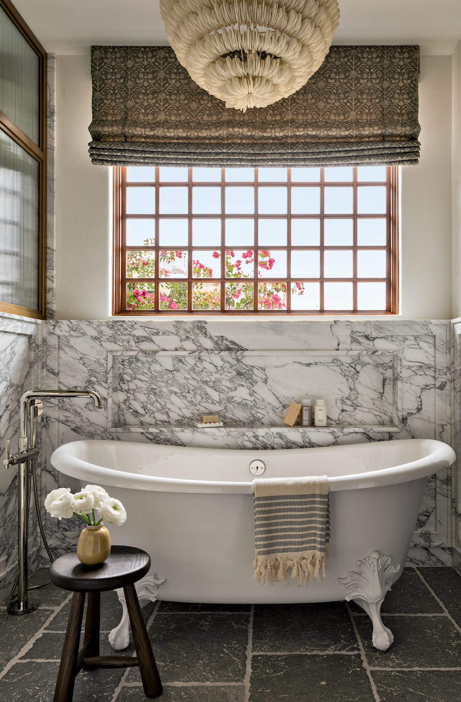 Elegant bathroom with a marble-clad clawfoot bathtub, striped towel, and a small stool