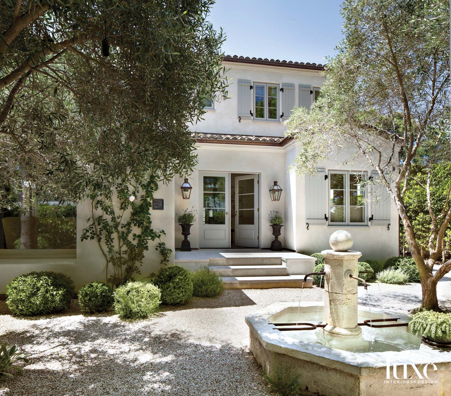 Front entrance to a French Provincial style home with a fountain at the front. House is painted white with blue shutters