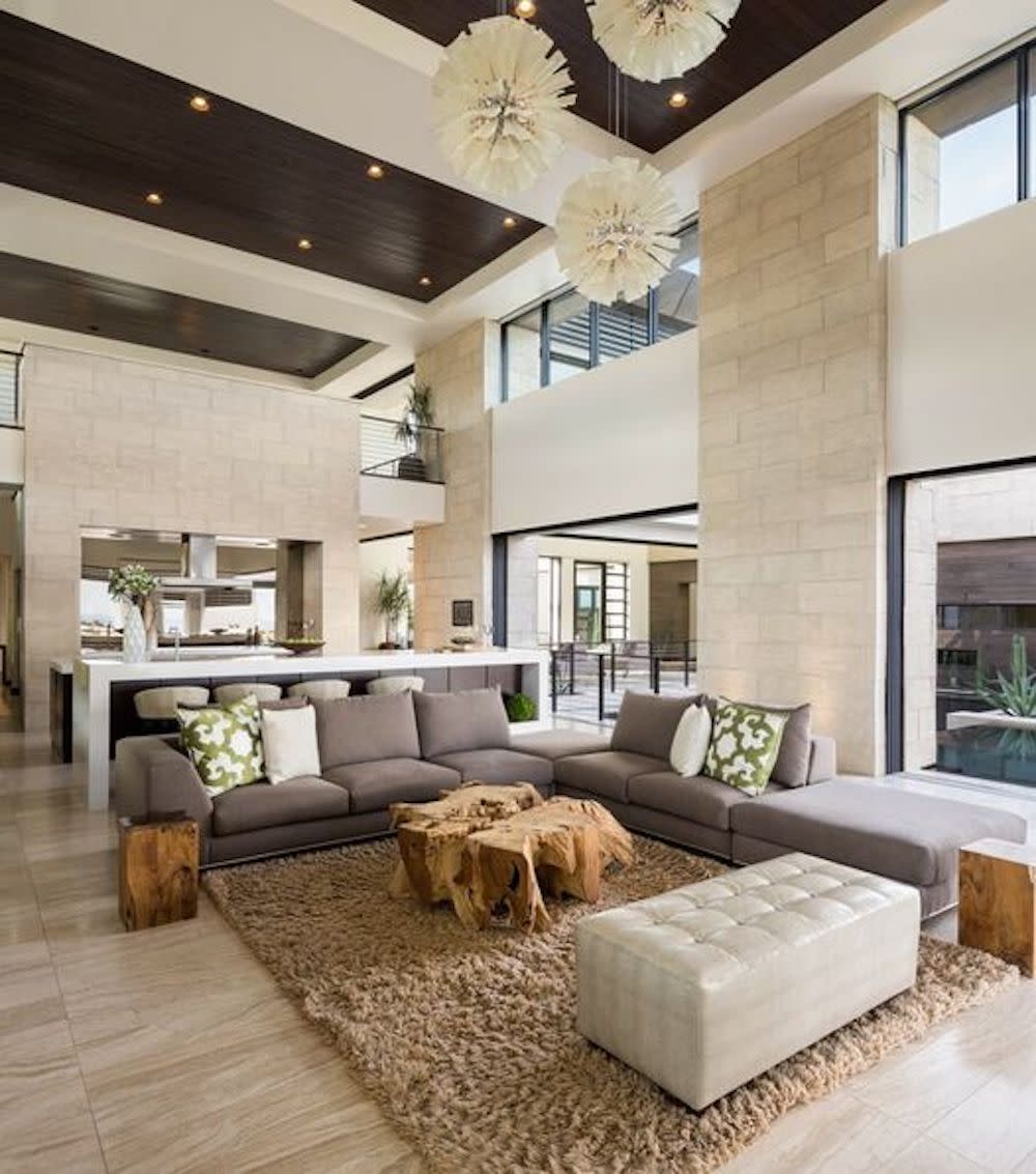 Open living space, with high ceiling, floor to ceiling windows and decorative, round, three piece chandelier.