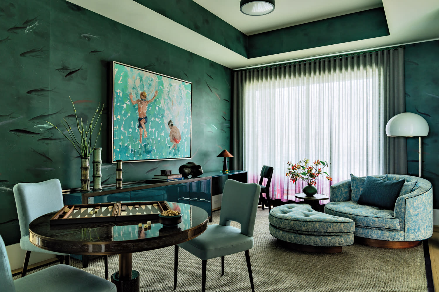 Sophisticated living room with teal walls and a large window with sheer curtains. Features a round table with backgammon, abstract art, and cozy seating.