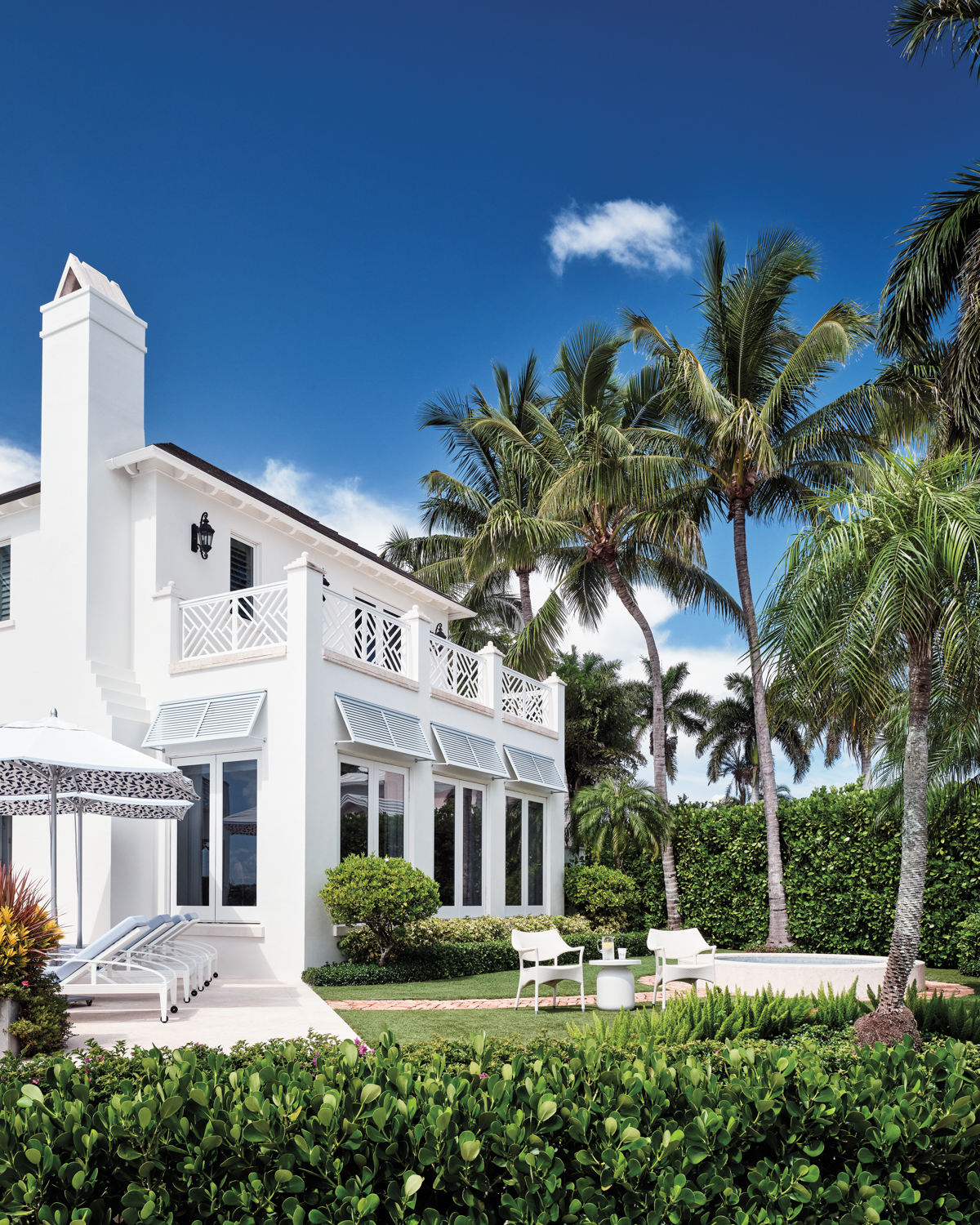 back exterior of a Naples house with a white facade, lush landscaping and palm trees