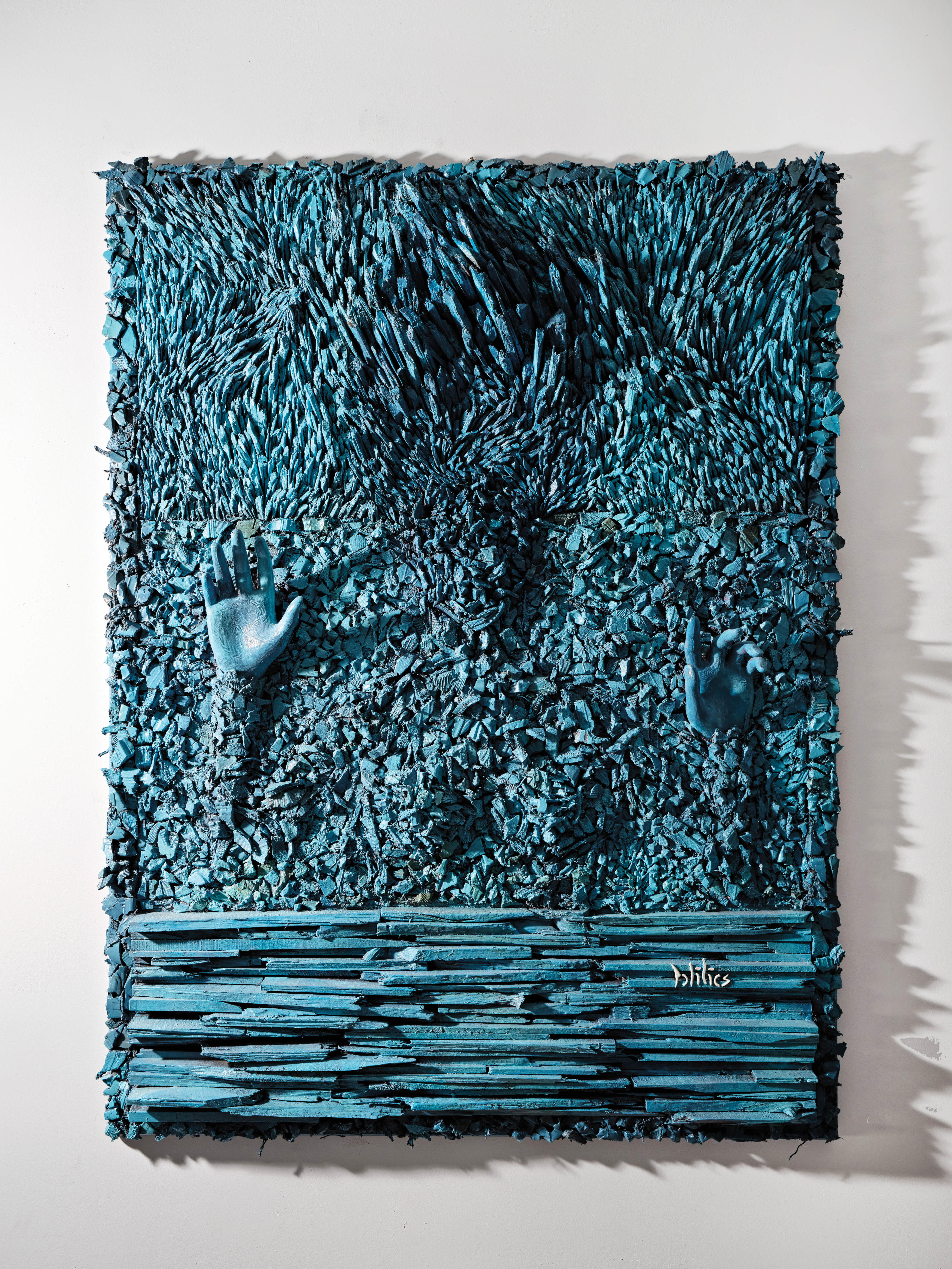 mixed-media artwork with hands pushing out of a blue relief