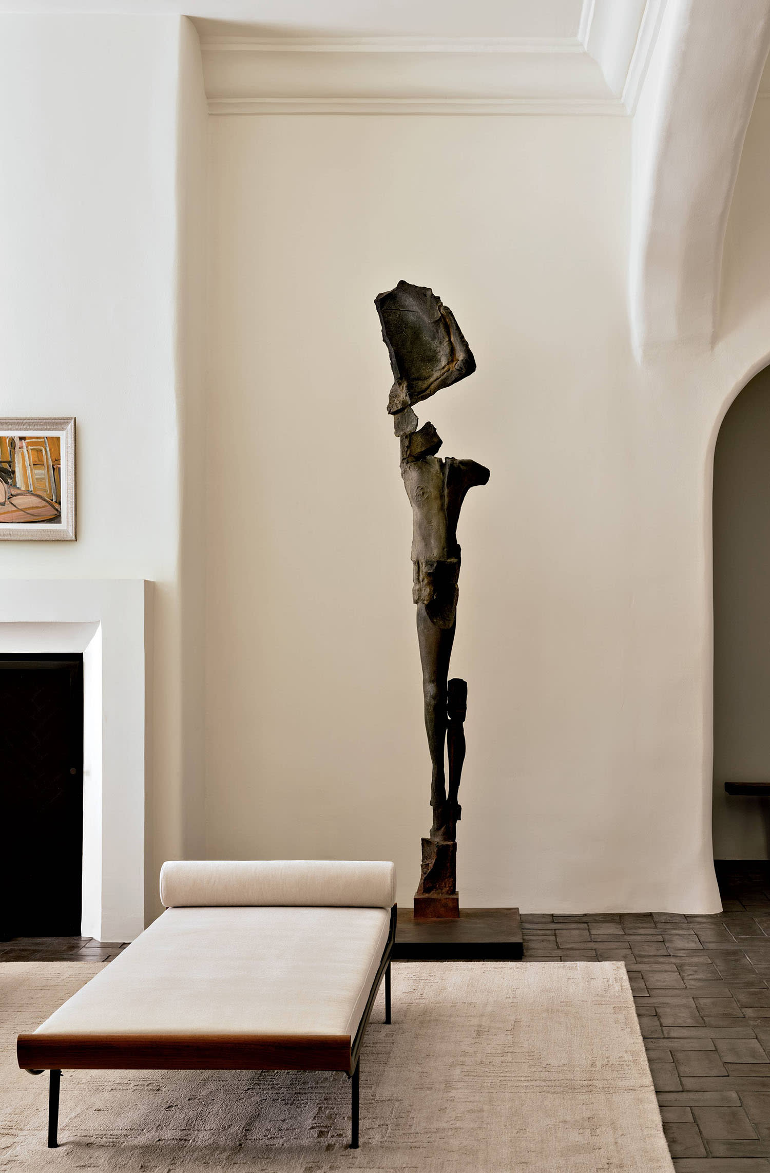 A sculpture sits next to a vintage daybed in light-colored fabric, with a coordinating rug underneath.