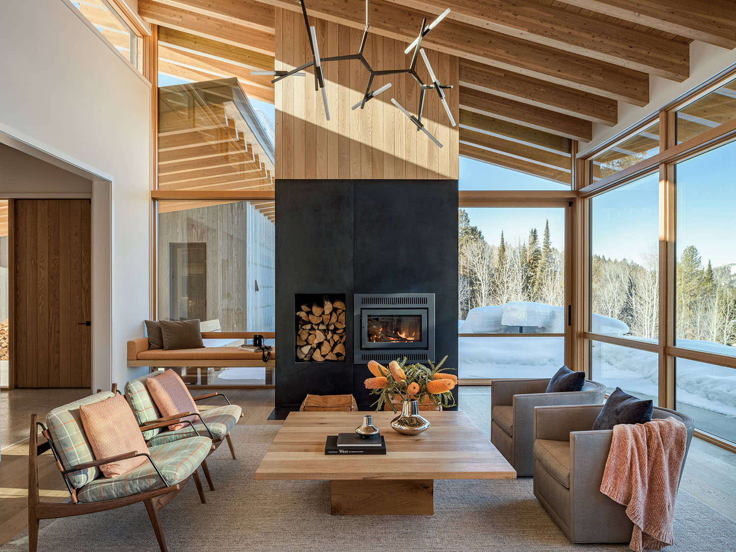A living room with a fire burning in the fireplace and four armchairs around a square coffee table.