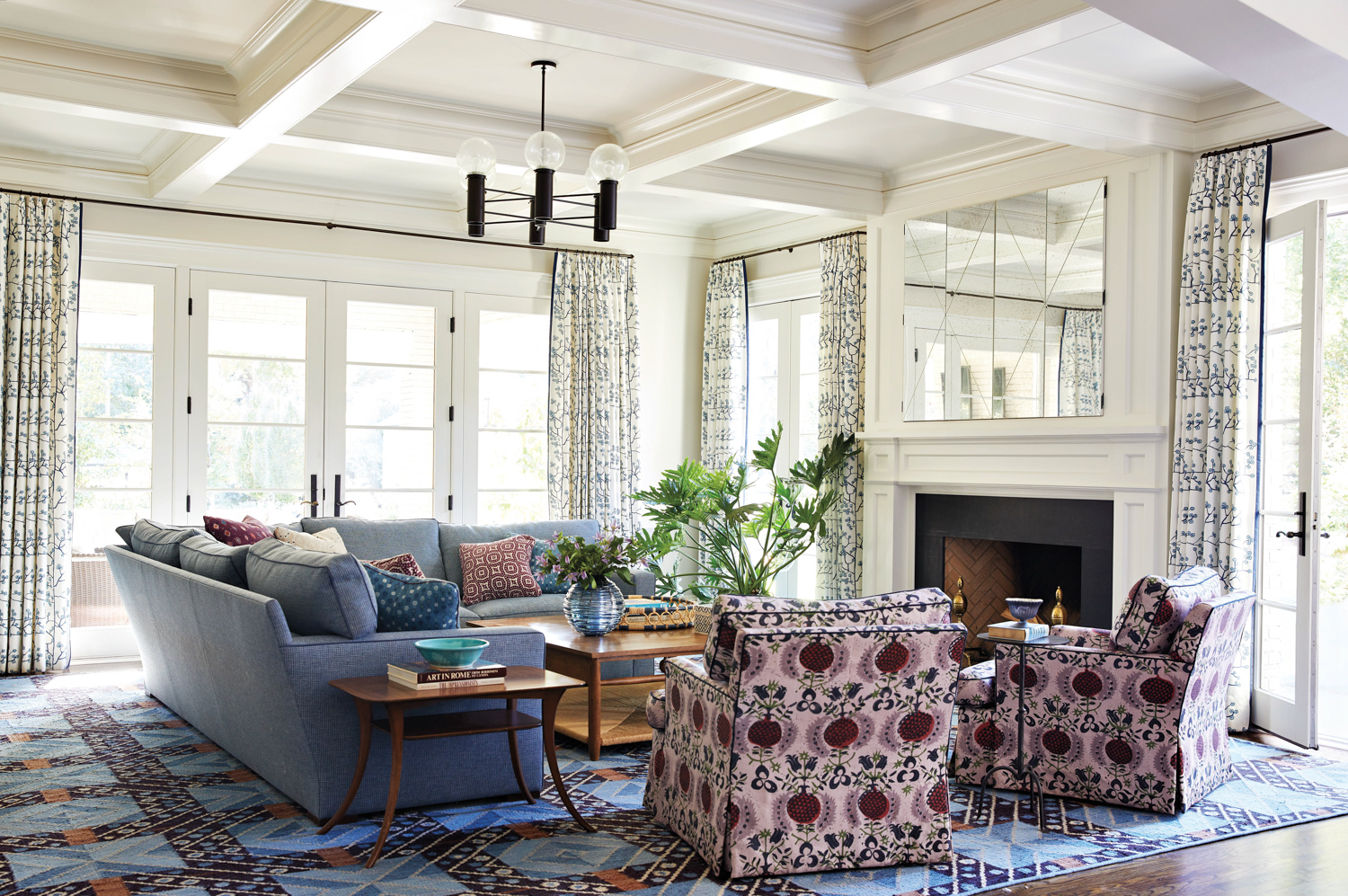 Family room with coffered ceiling, blue sofas and purple patterned armchairs by Story Street Studio