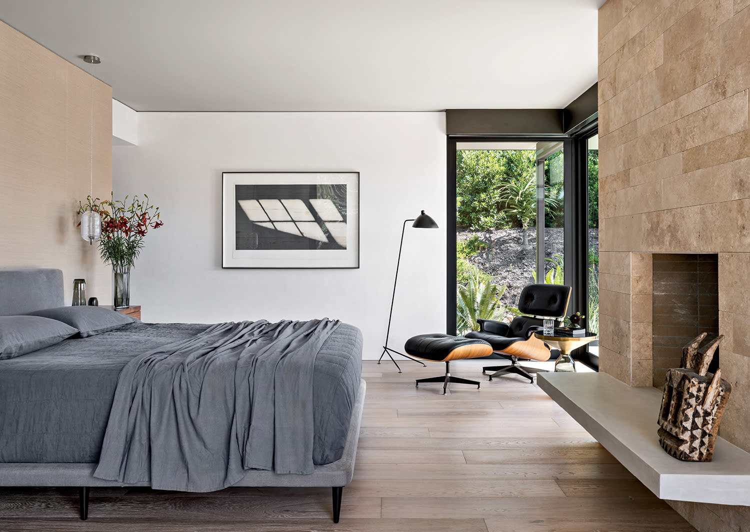 contemporary neutral bedroom with an Eames armchair and stone fireplace