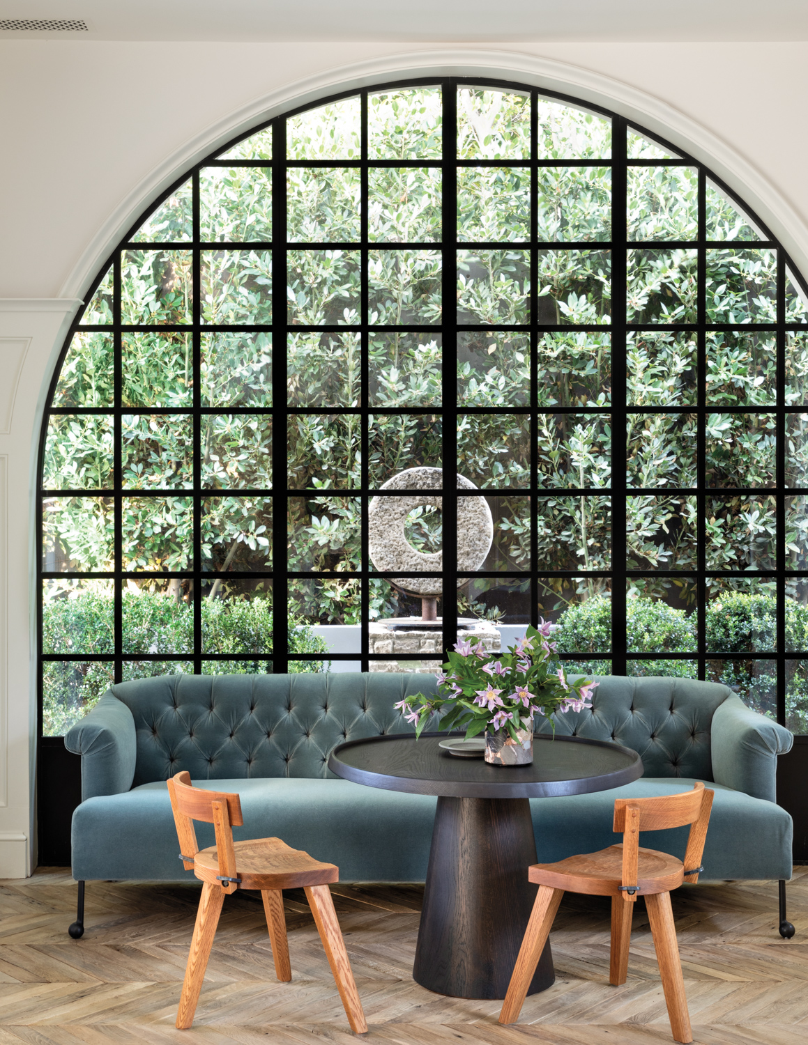 family room with large arched steel window fronted by blue sofa, round table and two chairs