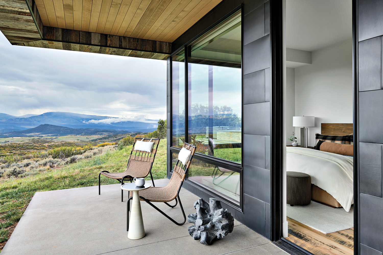 outdoor porch with tan lounge chairs, decorative teak ball and black shiplap walls