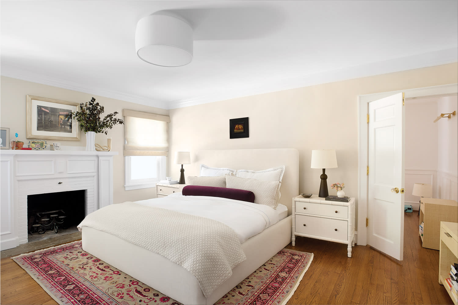 A cozy bedroom with a white bed, purple bolster, and plush pillows. 