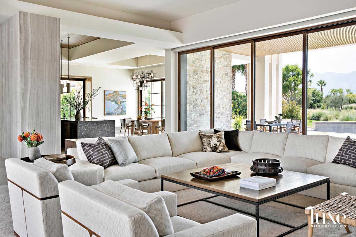 Living room with a sectional and pair of lounge chairs facing kitchen and terrace.