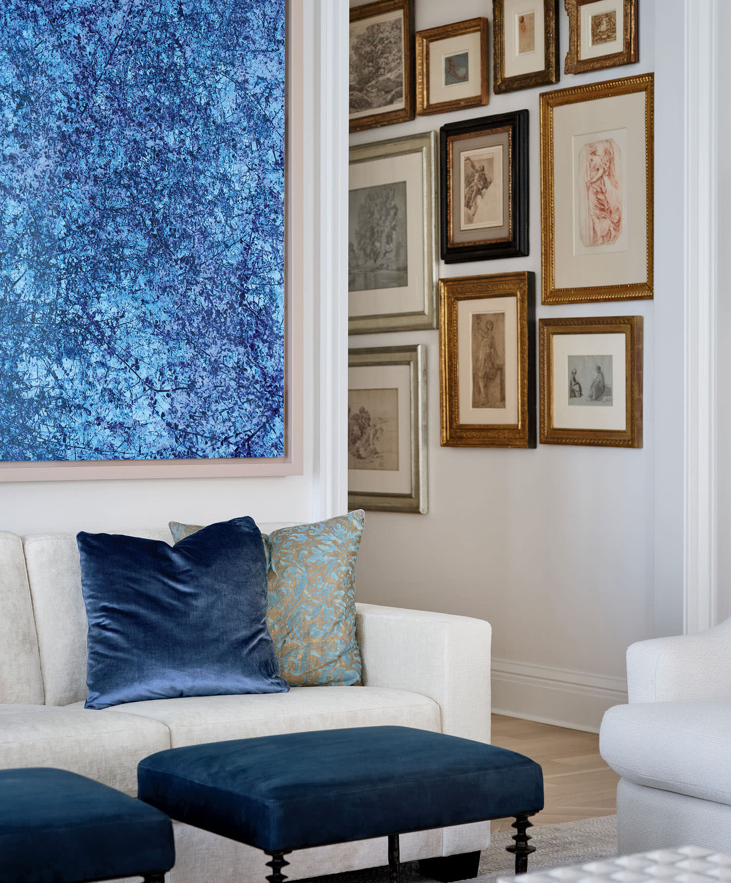A light-colored couch, with blue ottomans and accent pillows, sits beneath blue artwork on the wall.