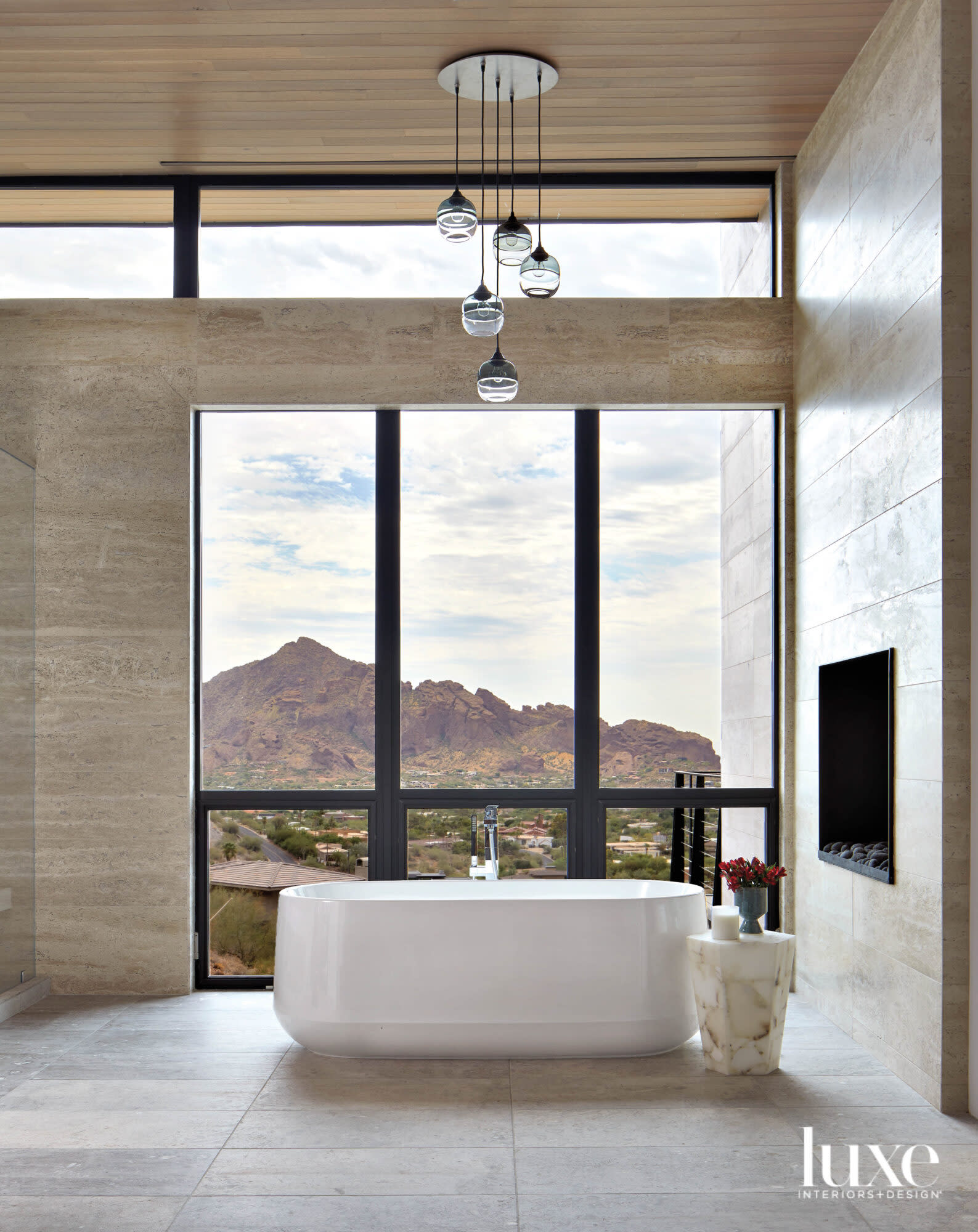 A bathroom with a large white standalone bathtub and floor-to-ceiling windows that look out on the mountains.