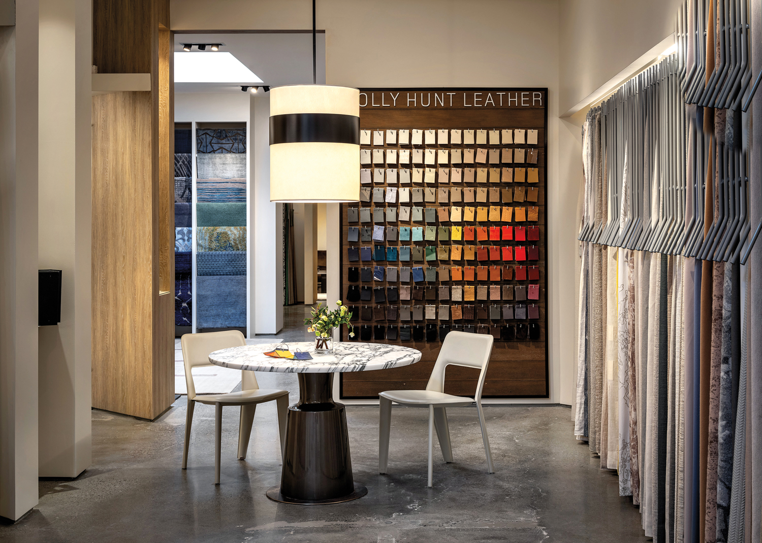 Showroom with a wall of leather samples behind a round marble-topped table and an oversize pendant light.