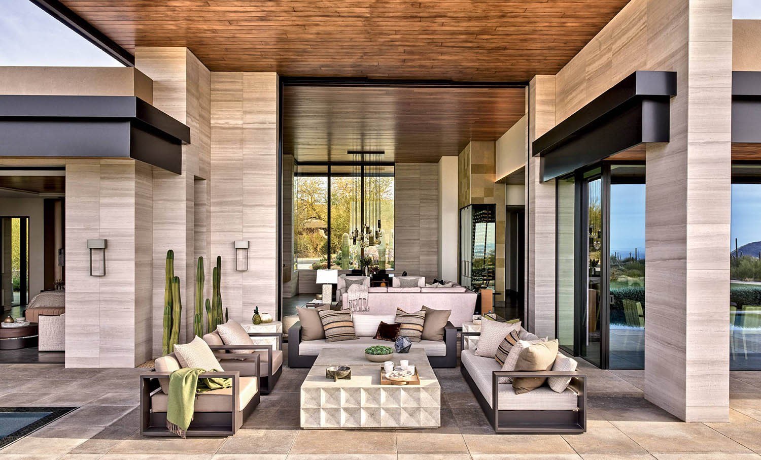 A pool terrace with couches and limestone floor tiles that extend into an indoor living room space.