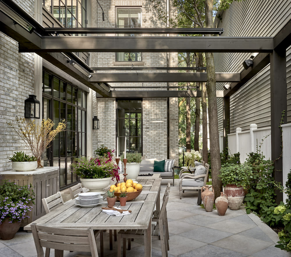 This outdoor living space is both comfortable and functional with teak dining table and chairs for outdoor meals and a separate seating area with couches and fire pit for cozy conversations.