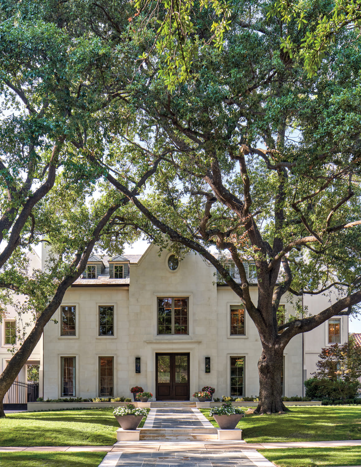 exterior of a home with a limestone facade framed by oak trees