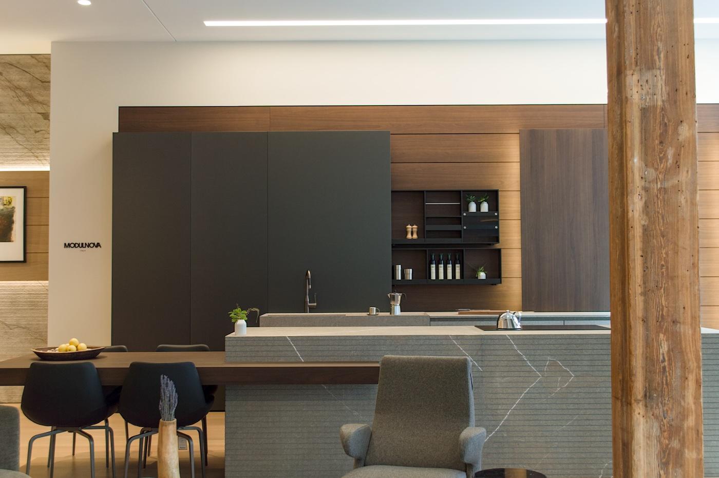 Modern kitchen with sleek design features dark cabinets, a marble island, and minimalistic decor. A tall wooden beam adds rustic contrast.